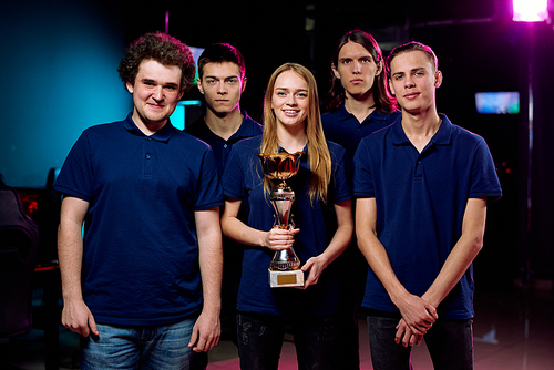 Portrait of positive best cybersports team in blue tshirts posing with winning award in computer club
