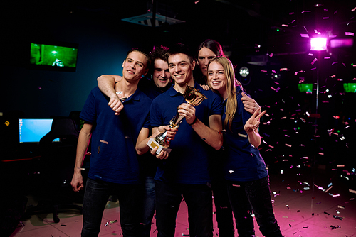 Happy team of young computer gamers winning golden cybersports Cup in competition and posing for group photo under confetti