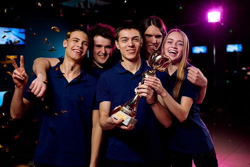 Team of excited teenage participants of e-sports video gaming competition standing in front of camera and showing prize for their victory