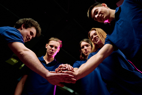Team of five successful young e-sports clubbers making pile of hands meaning support while standing in circle in front of camera