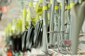 Metallic rakes, shovels and other gardening worktools hanging in row inside large contemporary farming supermarket for garden lovers