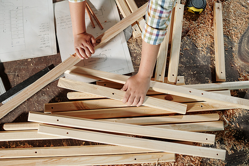 Above view of unrecognizable boy using sketches while assembling furniture in carpentry workshop