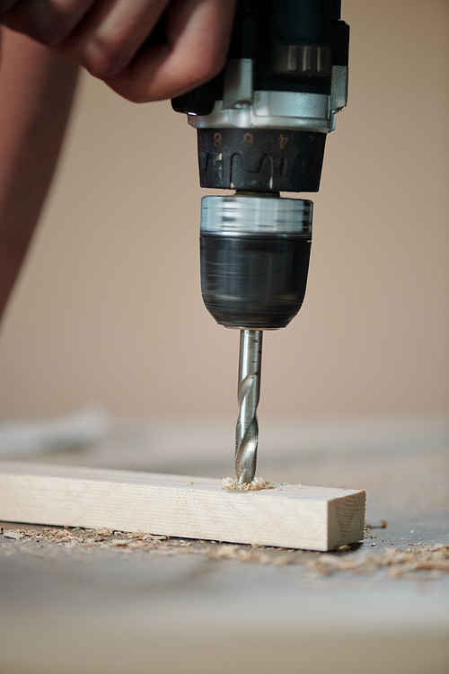 Close-up of unrecognizable furniture maker drilling wooden plank in joinery workshop