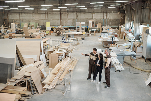 Group of workers of contemporary factory discussing furniture producing materials while sales manager pointing at them at meeting