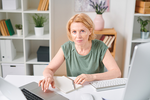 Mature businesswoman with undereye patches looking at you while networking in front of laptop during home quarantine