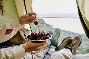 Close-up of unrecognizable couple sitting in camping tent at lake and eating ripe cherries