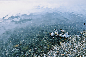 Pebbles under pure transparent water of lake or river and part of bank consisting of stones of various shapes and sizes
