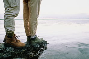 Close-up of unrecognizable couple in hiking boots standing on rock and contemplating waterscape