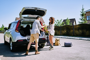Young couple of hikers loading stuff into car trunk while preparing for trip together