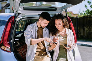 Young man pointing at map in smartphone while explaining his wife where they are going to move and showing her place to stop for rest