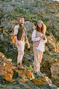 Content active young couple in comfortable wear walking over stone rocks while hiking together