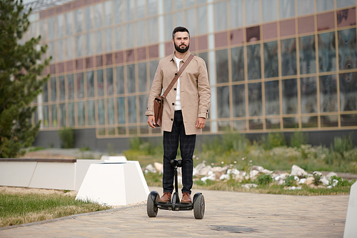 Contemporary young elegant businessman standing on gyroscope while moving in urban environment against modern architecture