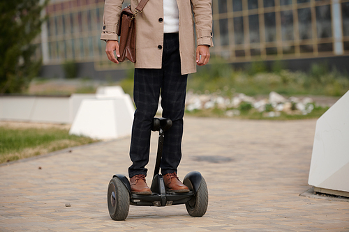 Front view of young contemporary elegant man with leather bag standing on gyroscope and moving to business center in the morning