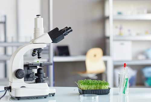 Background image of electronic microscope and plant saplings on equipment table in biotechnology lab, copy space