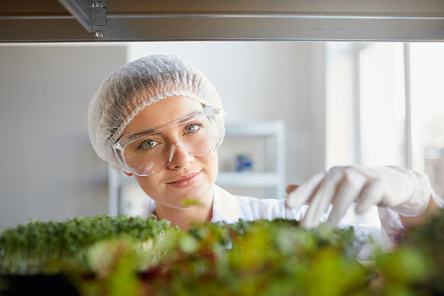 Close up portrait of young female scientist looking at camera and examining plant samples while working in biotechnology lab, copy space