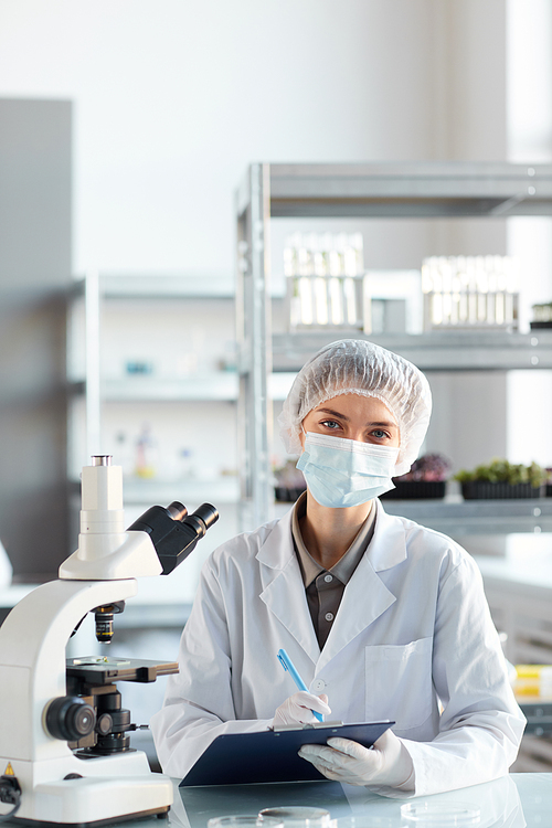 Vertical portrait of young female scientist wearing face mask and looking at camera while working in laboratory, copy space above