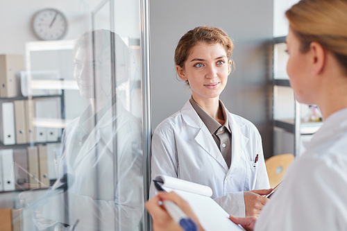 Waist up portrait of two female scientists writing on glass wall and holding clipboard while doing research in medical laboratory, copy space