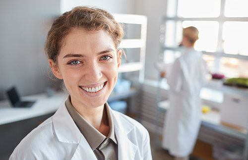 Close up portrait of young female scientist looking at camera and smiling while standing n medical laboratory, copy space