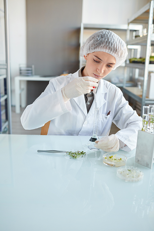 Vertical portrait of young female scientist performing experiments with plant samples while working on research in biotechnology lab, copy space