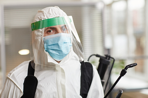 Portrait of male disinfection worker wearing full protective gear and looking at camera while sanitizing office, copy space