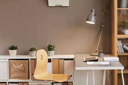 Minimal background image of cozy workplace lit by warm lighting from metal desk lamp, copy space