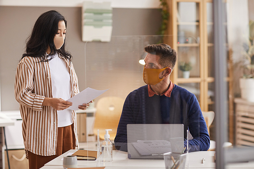 Two business people wearing face masks while discussing project in office, copy space