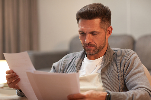 Portrait of handsome mature man looking at documents while working from home, copy space