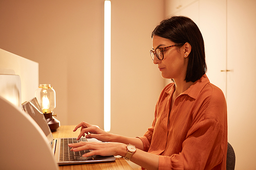 Side view portrait of adult businesswoman using laptop while working at desk in minimal futuristic interior, copy space