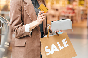 Close-up of unrecognizable woman in velvet jacket holding credit card and purse while preparing to spend money for shopping