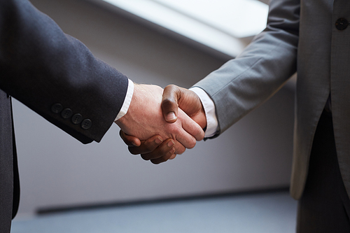 Close up of unrecognizable successful businessman shaking hands with African-American partner after closing deal, minimal background in grey tones, copy space