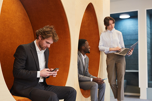 Multi-ethnic group of young business people working in contemporary office interior or coworking center, focus on bearded man using smartphone in foreground, copy space