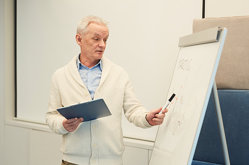 Waist up portrait of modern white-haired businessman standing by board in conference room while giving presentation or seminar, copy space