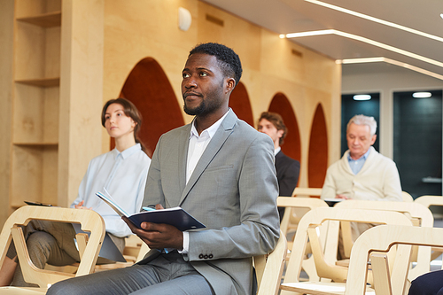 Portrait of African-American businessman taking notes while sitting in audience of contemporary conference hall interior, copy space