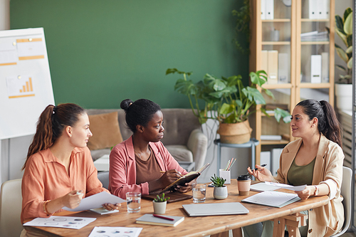 Portrait of female business team discussing project while sitting at meeting table in conference room, copy space