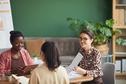 Portrait of smiling businesswoman presenting plans and charts while heading business meeting in office, copy space