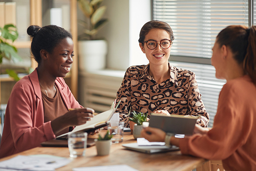 Portrait of successful female business team discussing work at meeting table and smiling cheerfully