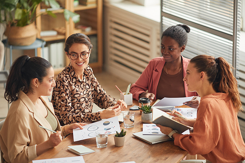 High angle portrait of successful female business team discussing work at meeting table and smiling cheerfully, copy space