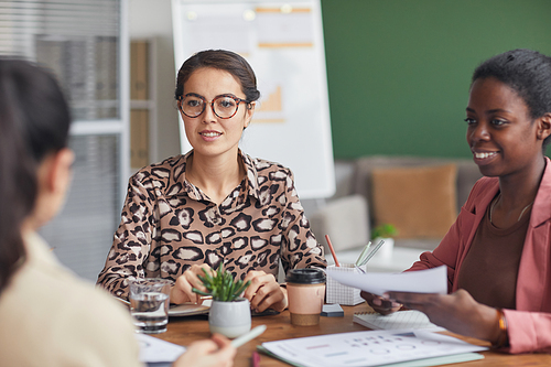 Portrait of young businesswoman wearing glasses while leading meeting with female business team in office