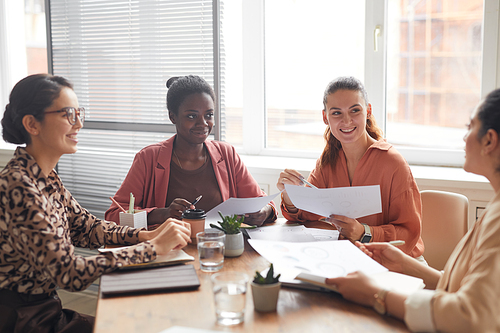 Portrait of multi-ethnic female business team discussing project while sitting at meeting table by window in office