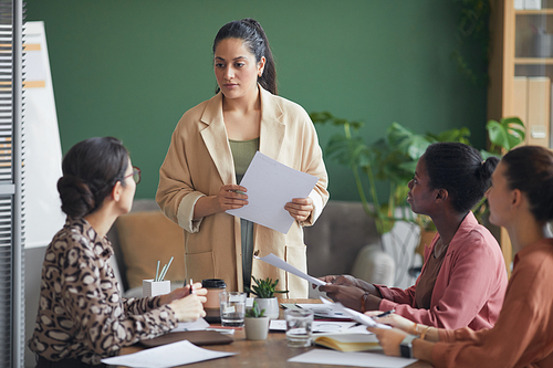 Portrait of successful female boss holding document while heading meeting with business team in office, copy space