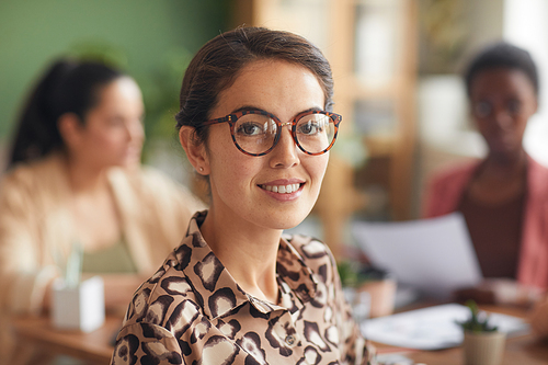 Close up portrait of elegant businesswoman wearing glasses and smiling at camera with female team in background, copy space