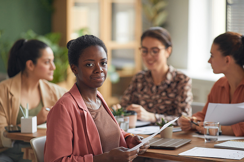 Portrait of contemporary African-American businesswoman smiling at camera with female business team in background, copy space