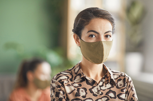 Portrait of elegant businesswoman wearing mask and looking at camera while standing against business meeting in office, copy space