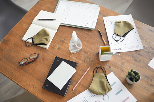 Top view background image of wooden meeting table with documents, masks and hand sanitizer in office, copy space