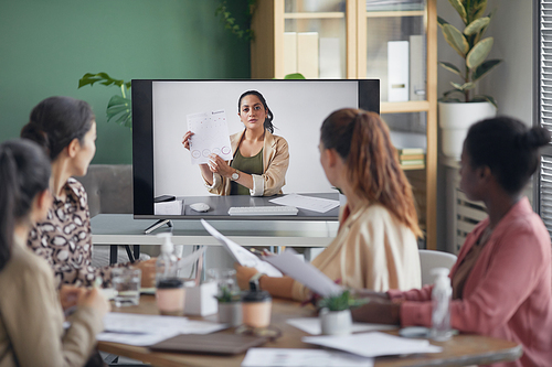 Portrait of businesswoman on computer screen talking to team and showing document during online business meeting in office, copy space