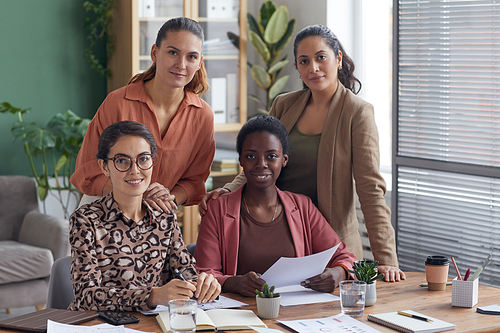Multi-ethnic group of four contemporary businesswomen smiling at camera while posing in office