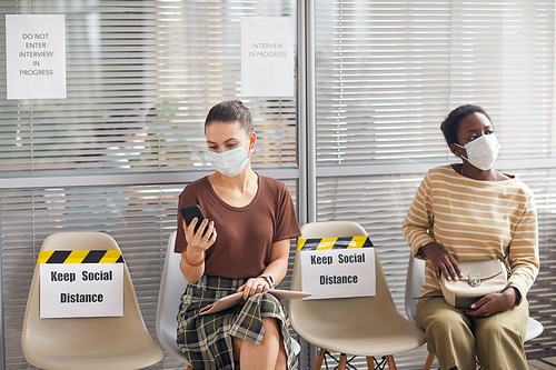 Portrait of two women wearing masks while waiting in line in office with Keep social distance sign during epidemic, copy space