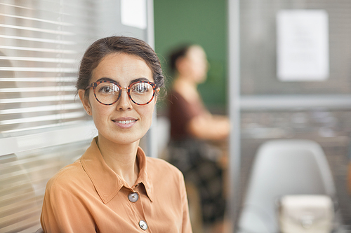 Portrait of modern young businesswoman wearing glasses and smiling at camera while waiting in line in office, copy space