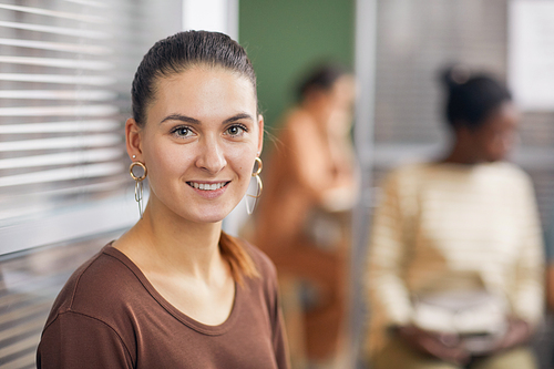 Portrait of smiling adult woman looking at camera while waiting in line in office, copy space