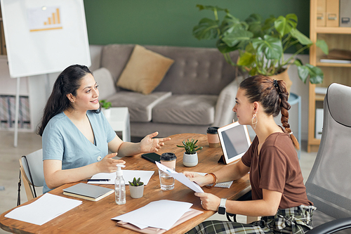 Portrait of young woman gesturing while talking to HR manager during job interview meeting in office, copy space